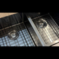 Load image into Gallery viewer, Close-up of a stainless steel kitchen sink with two round drain strainers and a grid-style drain cover.