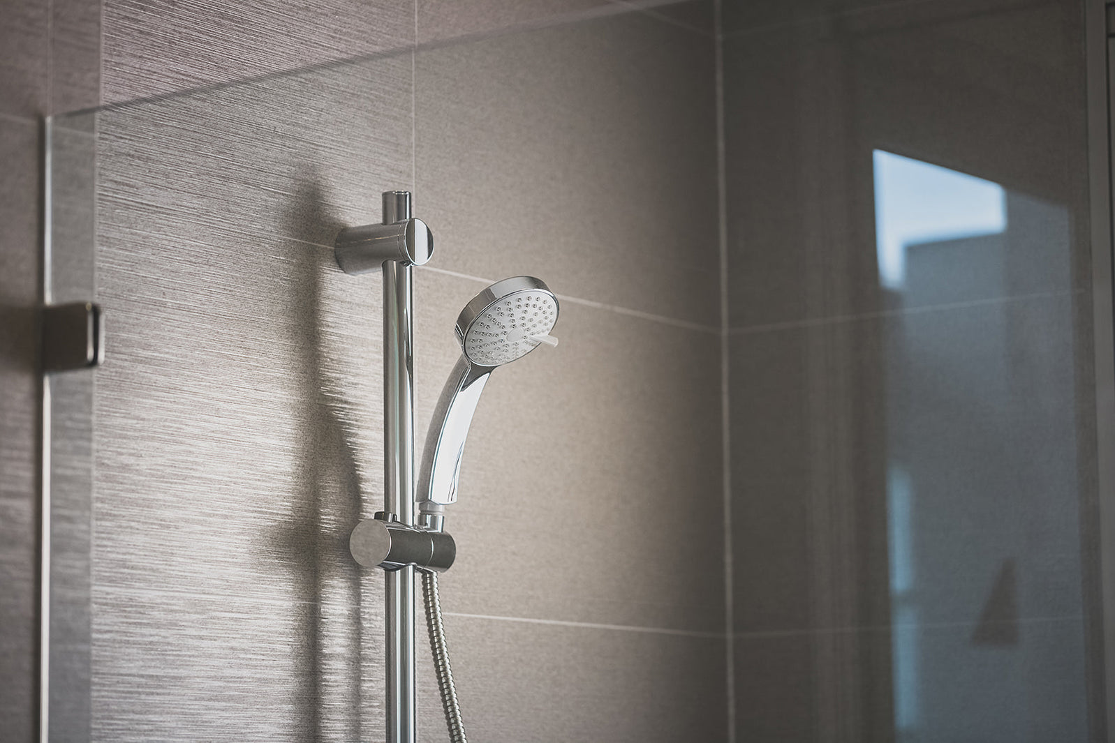 Chrome hand shower mounted on a shower rail in a tiled bathroom