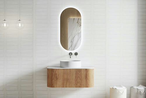 Bathroom with wooden vanity and oval mirror against a white tiled wall.