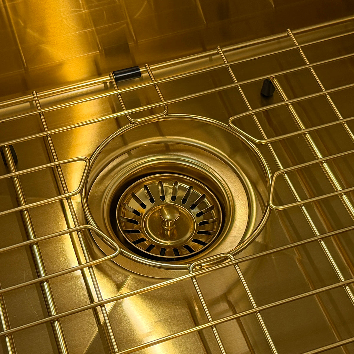 Close-up of a brushed brass or gold-toned metal sink drain basket with a circular strainer basket and wire grid over a matching gold-toned sink basin.